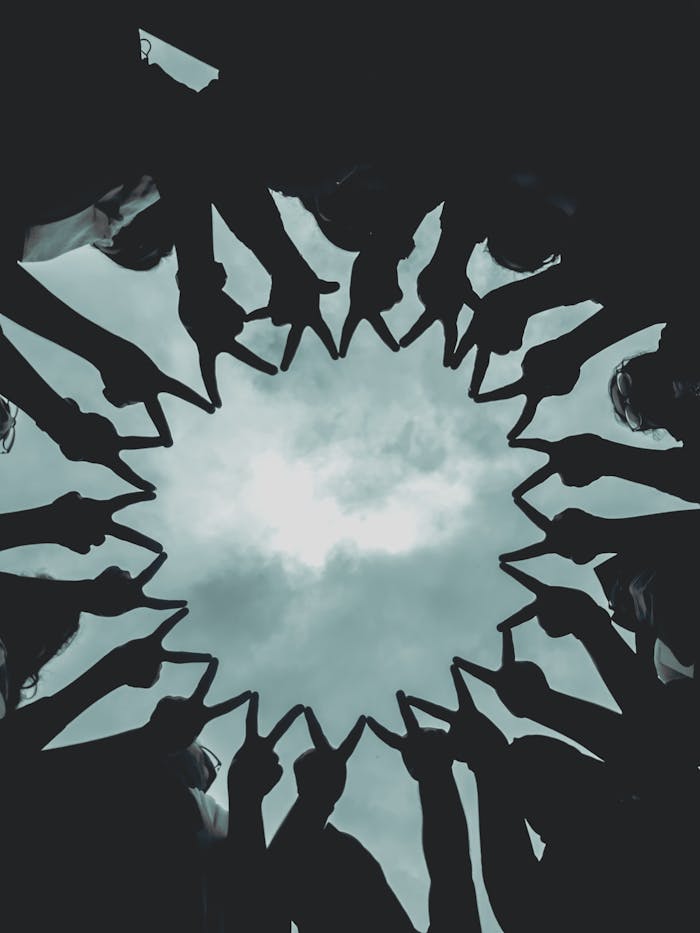 Services-01 Silhouette of people forming a star with hands against a cloudy sky.